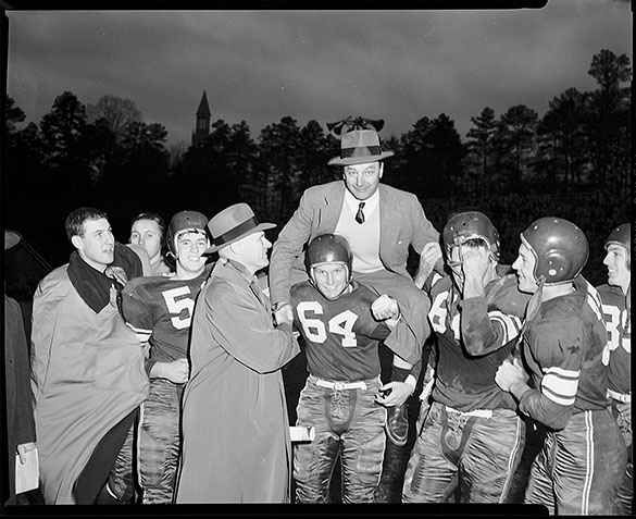 Duke head football coach Bill Murray being carried on shoulders of Duke football players, while UNC head football coach Carl Snavely shakes his hand at UNC-Chapel Hill versus Duke University football game at Kenan Memorial Stadium, Chapel Hill, NC. Duke players: #64 End Joe Hands, #39 Back David Lerps, #66 Guard Bobby Burrows, and #53 Center John Palmer.