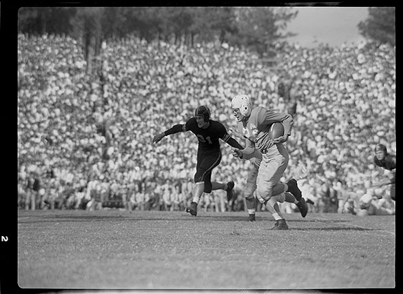 UNC tailback Charlie Justice, running with the ball, and Wake Forest defender Tom Fetzer at Groves Stadium, Winston-Salem, NC. Photograph (cropped) appears in October 10, 1948 Wilmington SUNDAY STAR-NEWS with caption: Charlie "Choo Choo" Justice evades Deacon tacklers in one of the Tar Heels' touchdown drives. Fetzer, 31, failed to stop the star back. Justice was injured on the play when he was finally brought to the ground, but he returned to the game after a short rest."