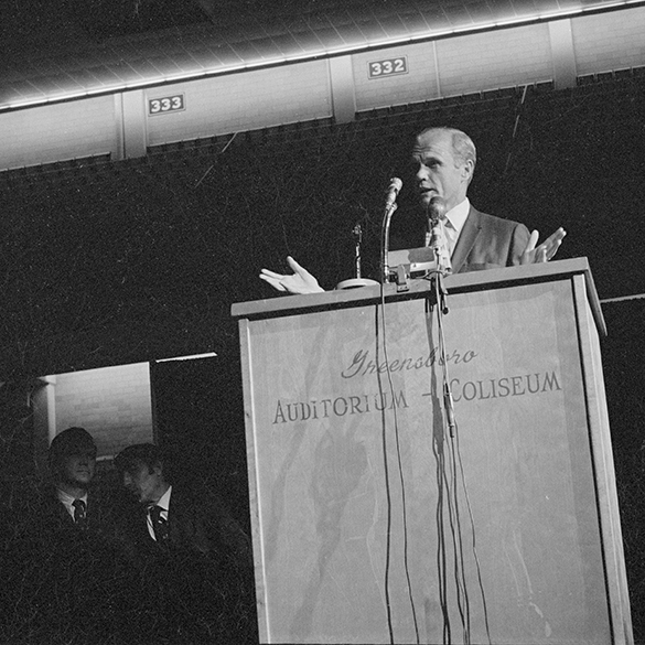 John H. Glenn Jr. addressing the audience at the Greensboro Coliseum, with other speakers waiting in the wings. Photographed using a off-angled perspective by Hugh Morton, cropped to a square format by the author.