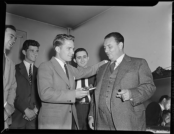 Leon Henderson (right), head of the Office of Price Administration established within the Office for Emergency Management of the United States Government by Executive Order 8875 on August 28, 1941. Henderson was the speaker for the Carolina Political Union's sixth anniversary on 15 April 1942 in Memorial Hall at the University of North Carolina at Chapel Hill. This photograph appears in the May 1942 ALUMNI REVIEW with caption headline "Have a Cigar!" and caption, "Evidently Price-Administrator Leon Henderson is not having to worry about cigar rationing. Here he is conferring with student leaders Ridley Whitaker, chairman of the Carolina Political Union, who hails from Goldsboro; Hobart McKeever of Greensboro, who was one of the candidates for presidency of the University Student Body; and Lou Harris of New Haven Conn., vice-president of the CPU. Mr. Henderson was one of the series of speakers brought to campus this year by student organizations." A slightly different Morton photograph of this group appeared in the 10 May issue of THE DAILY TAR HEEL.