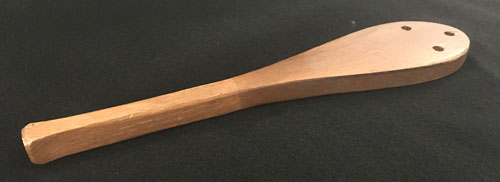Wood paddle shaped like a spoon with three holes in round part.