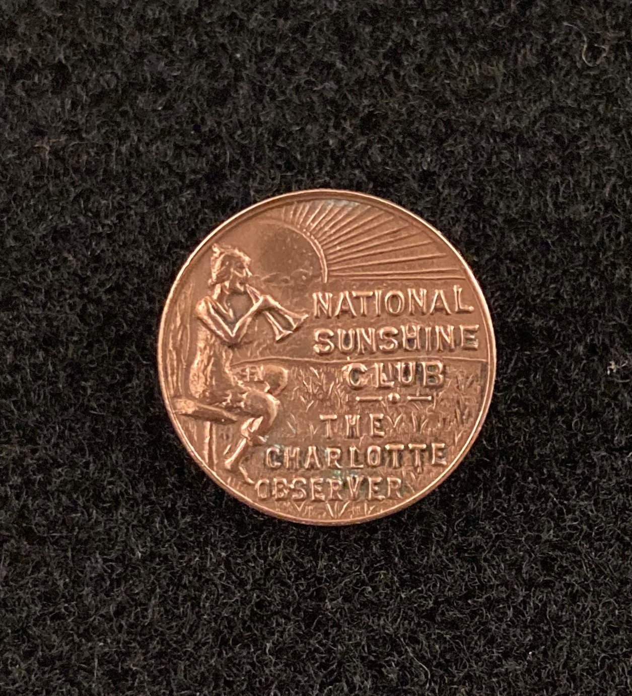 Pinback buton with image of person blowing on two horns and the words "National Sunshine Club, The Charlotte Observer."