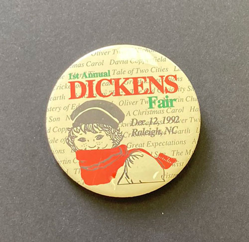 Pinback button for the first Dickens fair in Raleigh. The button includes an image of a young man wearing a 19th century cap and with a red scarf around his neck.