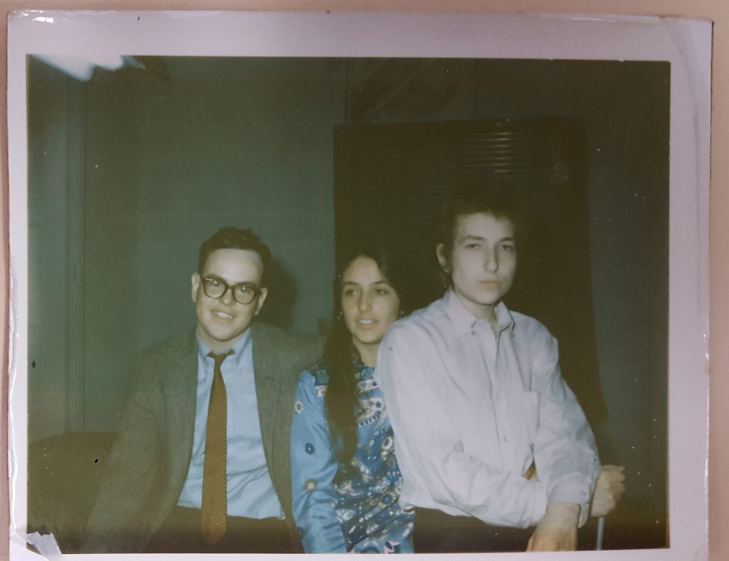 L to R: Bebo White in sport coat and tie, Joan Baez in blue blouse with flowers, and Bob Dylan in pinkish button down shirt with a scowl on his face