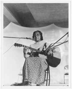 black and white photo of Elizabeth Cotten performing in a tent with her guitar.