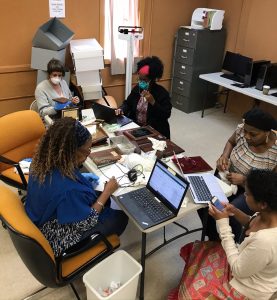 A majority Black group of women and femme-presenting people around a table working on labtops and looking at museum artifacts