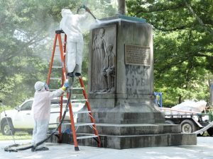 Workers in white protective clothing pressure clean the base of "Silent Sam."