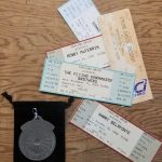 Multiple tickets on a brown wood surface, next to a black pouch with a circular silver item.