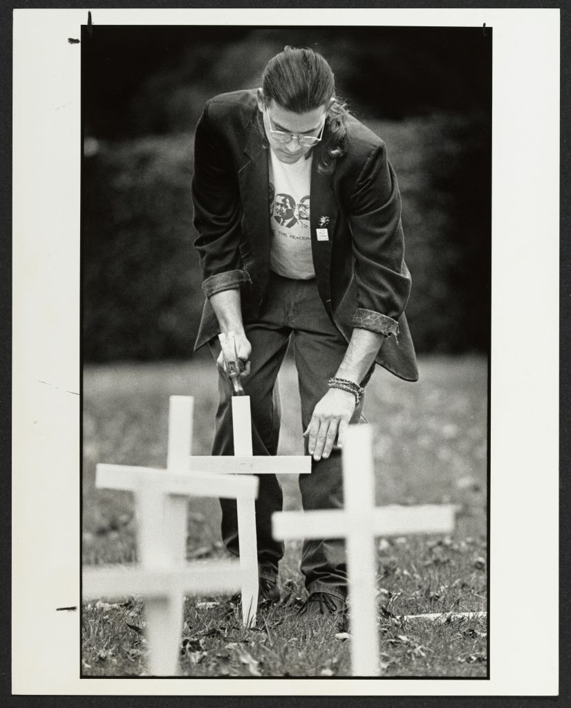 A student hammering a wooden cross in a grassy area of campus.