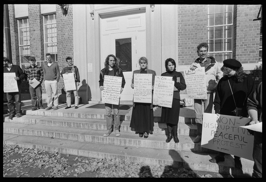 Ten students hold posters against the CIA's presence on campus in front of Hanes Hall